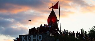 Festivalbesucher stehen auf einem alten Flugzeughangar neben einer beleuchteten Fusion-Rakete.