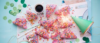 Einige Doughnuts, ein Pappbecher mit Kaffee, Partyhüte, Konfetti auf einem Tisch